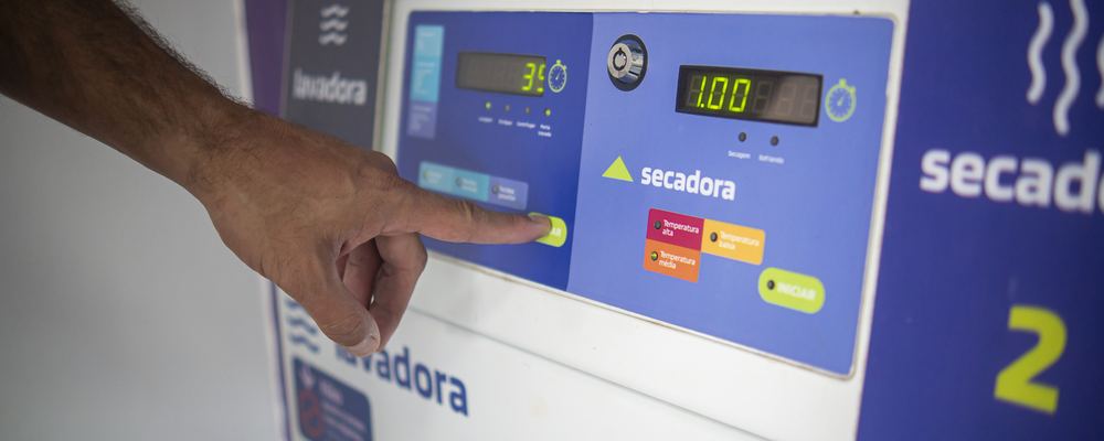Cliente apertando o botão de iniciar no painel de uma máquina da Lavô, com o display marcando 35 graus